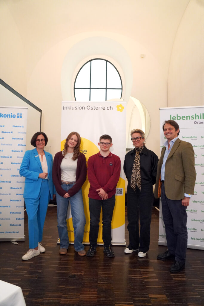 Fünf Personen stehen in einer Reihe vor zwei Veranstaltungsbannern mit Markenlogos.